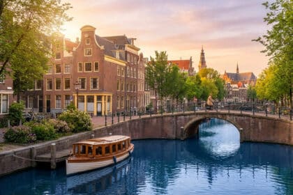 Canal d'Amsterdam au coucher du soleil. Un pont en briques, des maisons typiques, un cycliste et une péniche amarrée. Lumière douce.