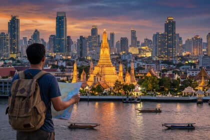Voyageur avec sac à dos et carte contemplant le Wat Arun illuminé et la skyline de Bangkok au crépuscule, rivière animée.