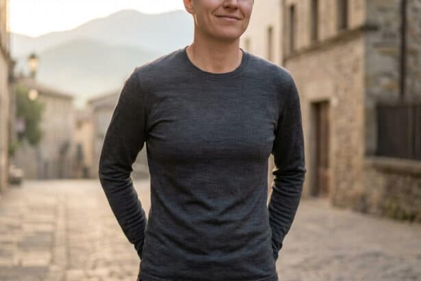 Femme portant un t-shirt à manches longues en laine mérinos gris foncé, souriante dans une rue pavée ancienne.