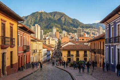 Vue d'une rue pavée et animée de La Candelaria à Bogotá, bordée de maisons coloniales colorées. La montagne Monserrate domine en arrière-plan.