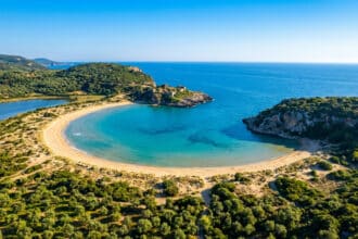 Vue aérienne de la plage de Voidokilia près de Pylos, Grèce : sable doré, eaux turquoise, lagon, ruines de château sur promontoire.