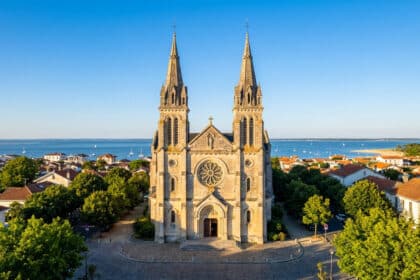 Vue aérienne de la basilique Notre-Dame d'Arcachon avec ses deux flèches dominant les toits et le Bassin d'Arcachon.
