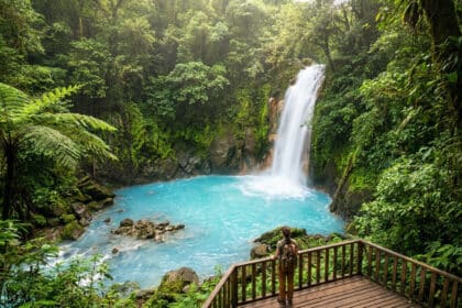 Une randonneuse contemple la cascade turquoise du Rio Celeste entourée d'une forêt tropicale luxuriante.