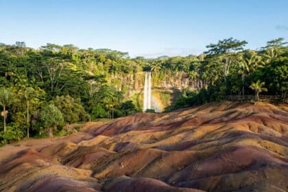 Vue panoramique des dunes de terre colorée de Chamarel à Maurice avec la cascade en arrière-plan sous un ciel bleu.