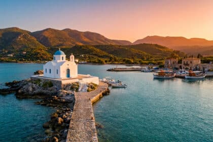 Petite église blanche à dôme bleu au bout d'une jetée en pierre à Georgioupolis, Crète, sous un coucher de soleil doré.