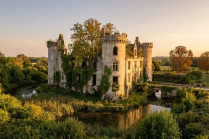 Vue aérienne du château de la Mothe-Chandeniers, envahi par la végétation au milieu de douves lors d'un coucher de soleil.