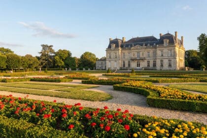 Le château de Peixotto entouré de jardins à la française fleuris sous un ciel bleu ensoleillé.