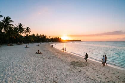 Vue panoramique d'une plage tropicale à Flic en Flac au coucher du soleil avec des personnes se promenant sur le sable.