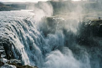 Vue panoramique de la puissante cascade de Dettifoss en Islande avec des touristes observant depuis le bord de la falaise.