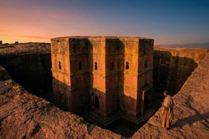 Vue panoramique de l'église monolithique Saint-Georges à Lalibela au coucher du soleil avec un fidèle en prière.