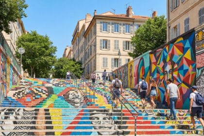 Escaliers peints de fresques colorées au Cours Julien avec des passants sous un ciel bleu à Marseille.