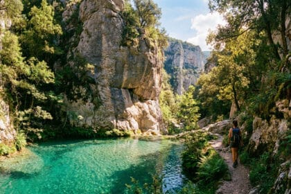 Randonneuse marchant près d'une vasque d'eau turquoise dans les Gorges d'Héric sous le regard d'un mouflon.