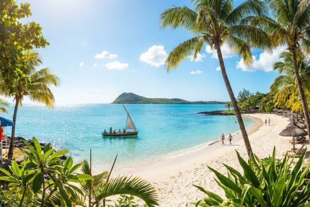 Vue panoramique d'une plage tropicale à Grand Baie avec un voilier traditionnel, des cocotiers et une eau turquoise.