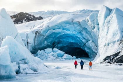 Trois personnes marchant vers l'entrée d'une grotte de glace bleue spectaculaire dans le glacier Vatnajökull en Islande.
