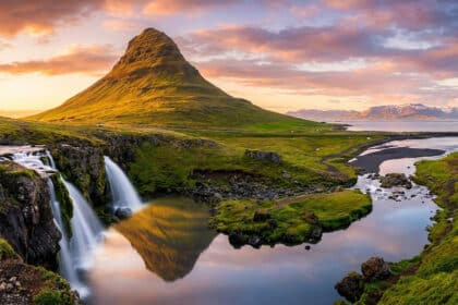 Chutes d'eau de Kirkjufellsfoss au pied de la montagne emblématique Kirkjufell sous un ciel coloré au coucher du soleil.