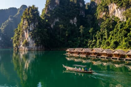 Bateau traditionnel thaï naviguant sur les eaux émeraude du lac Cheow Lan devant des bungalows flottants.