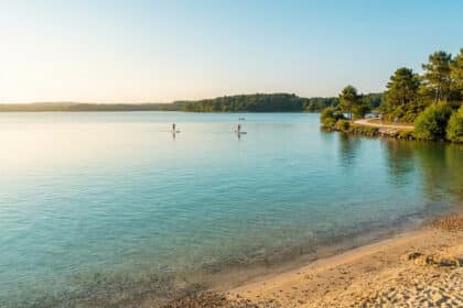 Vue panoramique du lac de Biscarrosse avec des personnes pratiquant le paddle sous une lumière douce de fin de journée.