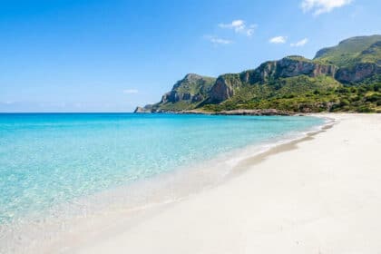 Plage de sable blanc et eaux turquoise cristallines à San Vito Lo Capo sous un ciel bleu ensoleillé.