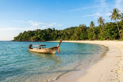 Bateau long-tail traditionnel amarré sur une plage de sable blanc et eaux turquoise à Koh Lipe, Thaïlande.