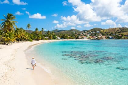Une personne marche sur une plage de sable blanc bordée de palmiers face à une mer turquoise en Guadeloupe.
