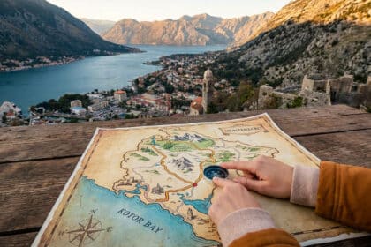 Mains consultant une carte et une boussole avec en arrière-plan une vue panoramique sur la baie de Kotor.