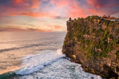 Temple d'Uluwatu perché sur une falaise surplombant l'océan Indien avec des surfeurs au coucher du soleil.