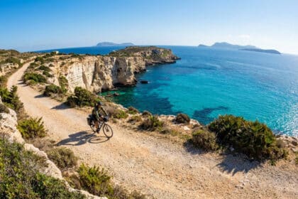 Un cycliste roule sur un sentier côtier en terre battue surplombant les eaux turquoise des îles Égades en Sicile.